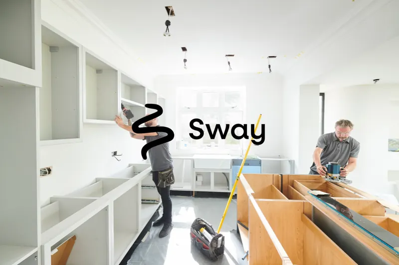 Two local tradesmen fitting a new kitchen, one fixing wall cabinets and the other routing a worktop