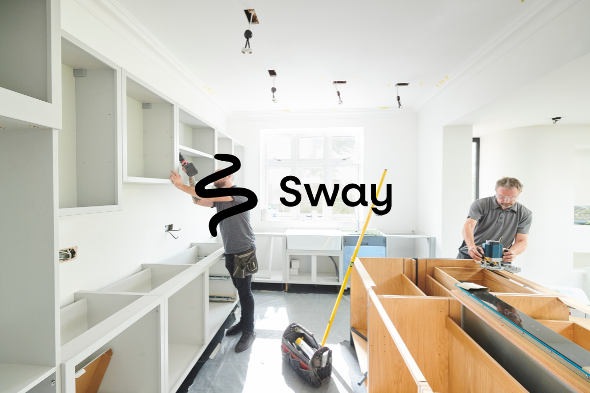 Two local tradesmen fitting a new kitchen, one fixing wall cabinets and the other routing a worktop
