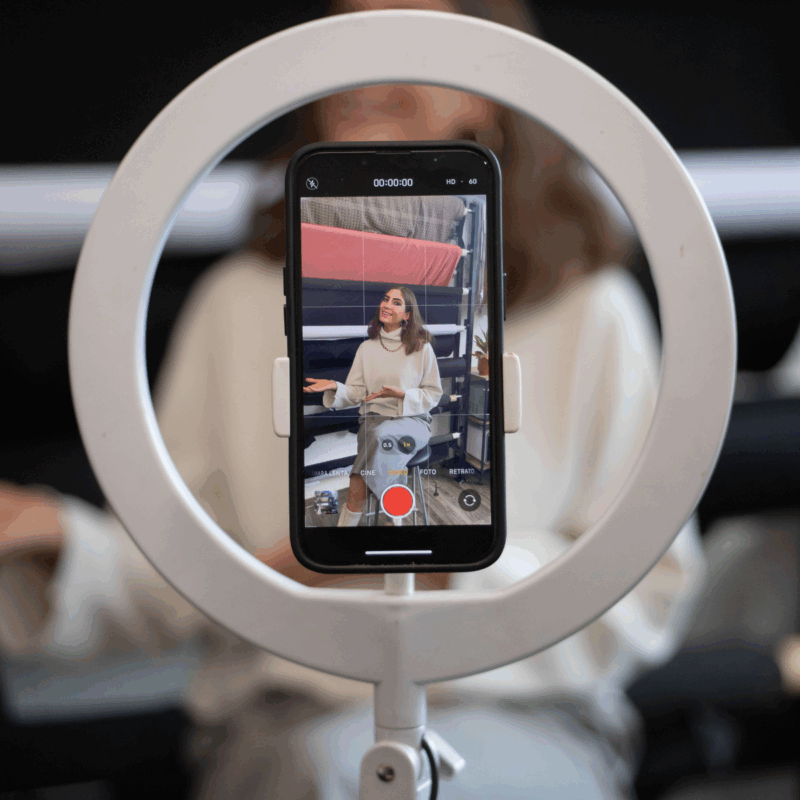 A phone mounted in a ring light, recording a woman filming user-generated content for social media