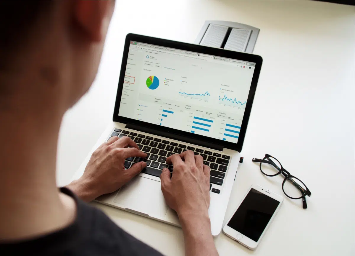 Person typing on a laptop showing a Google Analytics dashboard with a pie chart and traffic graphs