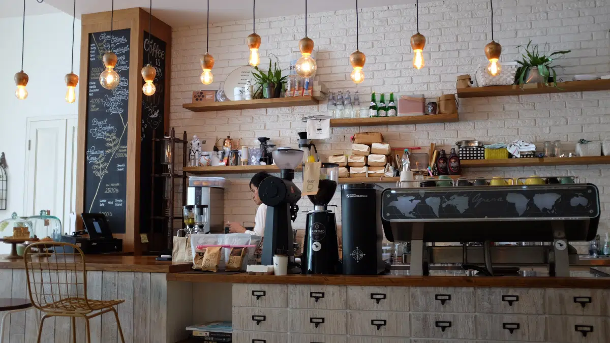 Barista working behind the counter of a coffee shop with exposed brick and hanging bulb lights