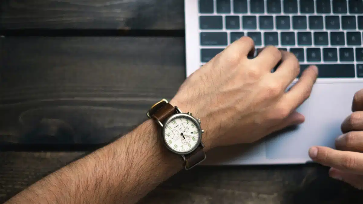 Close-up of a wrist watch next to hands typing on a laptop