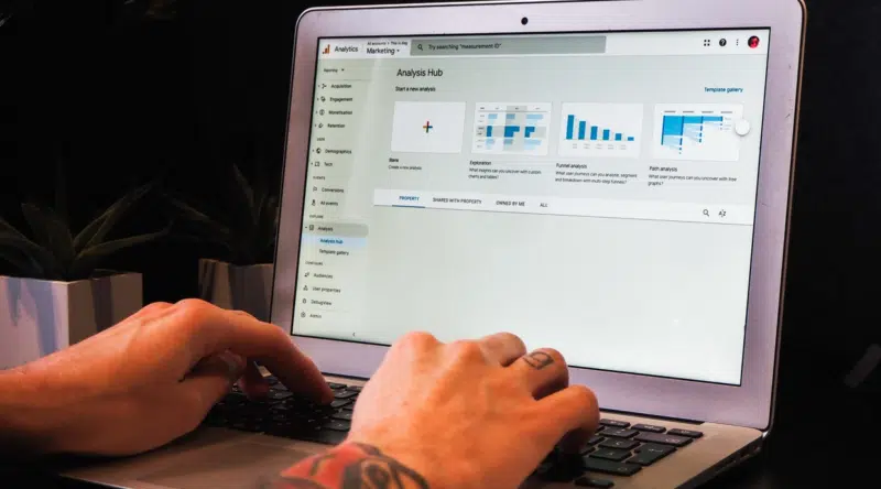 Person typing on a laptop showing the GA4 Analysis Hub interface with exploration, funnel, and path analysis templates