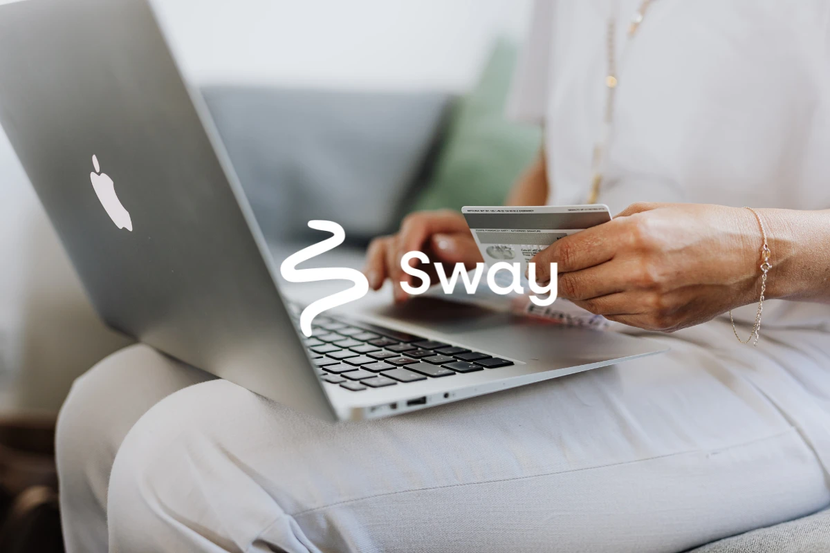 A woman sitting on a sofa with a laptop, holding her payment card to complete an online purchase